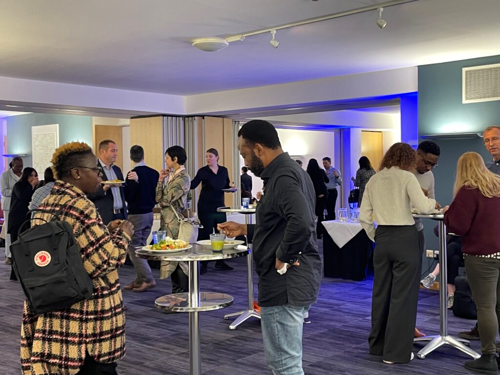 People gather around high tables, eating lunch and networking at an event space