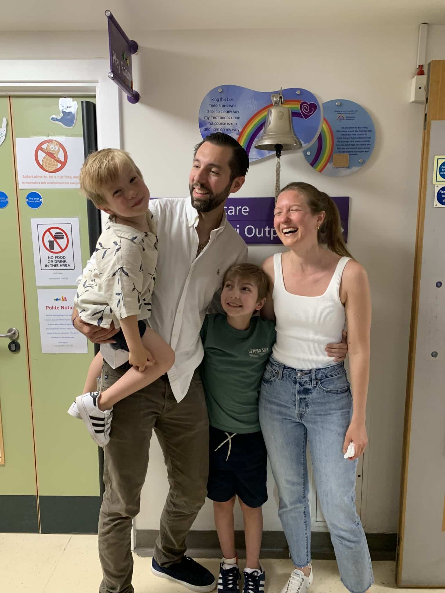 A family stand laughing in ward underneath a treatment bell